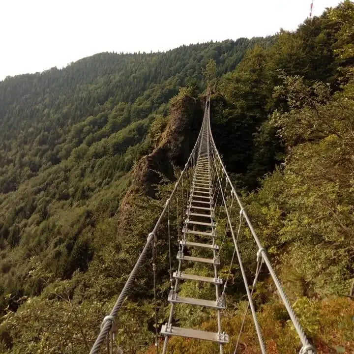A narrow suspension bridge stretching across a lush green mountain ridge near Kremnica, offering a thrilling hiking experience