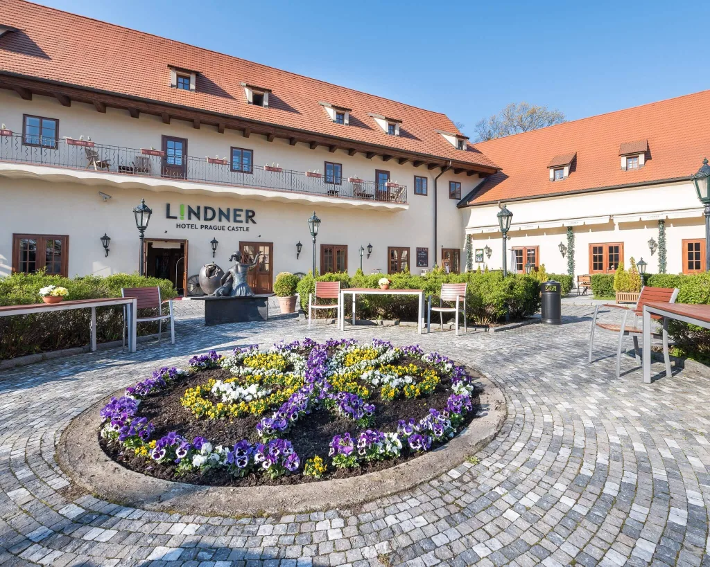 Courtyard of Lindner Hotel Prague Castle with blooming flowers and historical architecture on a sunny day.
