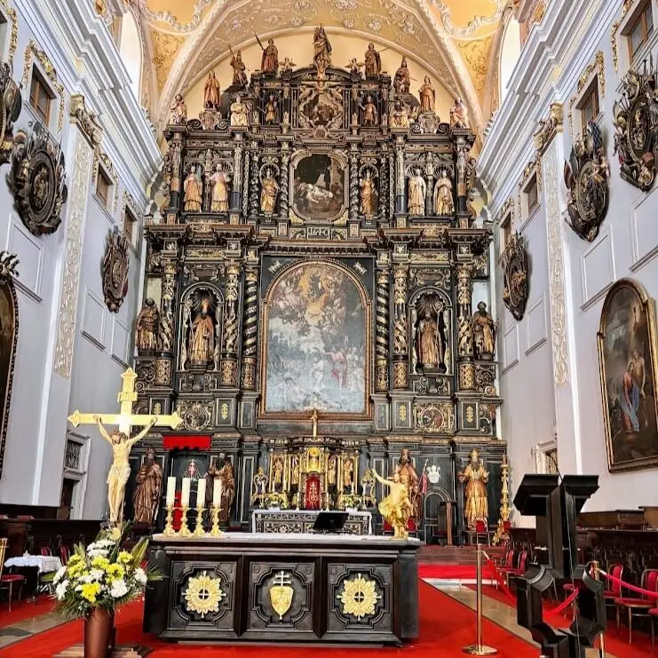 Explora Trnava: Impresionante altar mayor barroco negro y dorado en el interior de una iglesia histórica de Trnava, con esculturas religiosas, lienzos y alfombra roja en el presbiterio.