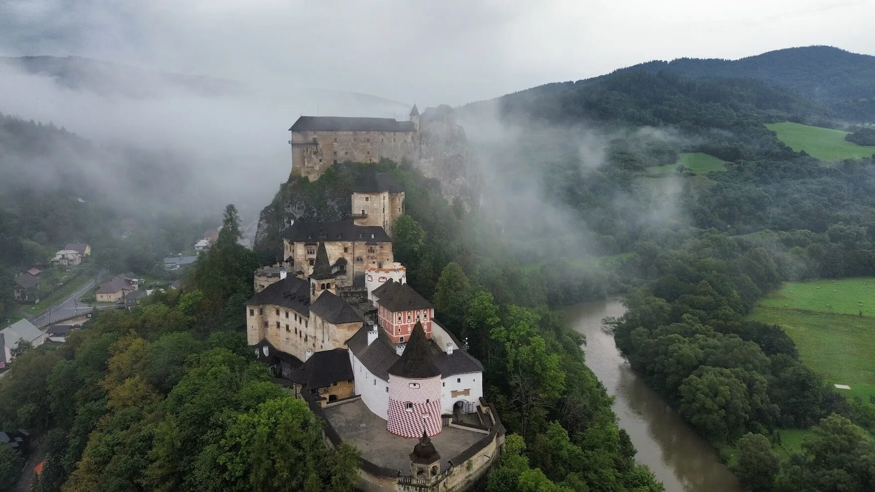 Le château d'Orava se dressant sur son rocher au-dessus de la rivière, vu du ciel à travers la brume matinale.