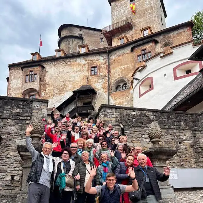 Un grand groupe de touristes saluant de la main depuis les marches en contrebas du château d'Orava, en Slovaquie.