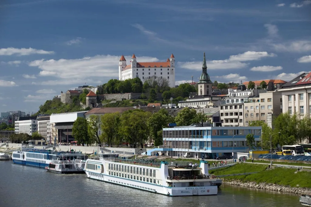 River cruise ships moored along the Danube in Bratislava, with the castle and the old town on the hill behind.