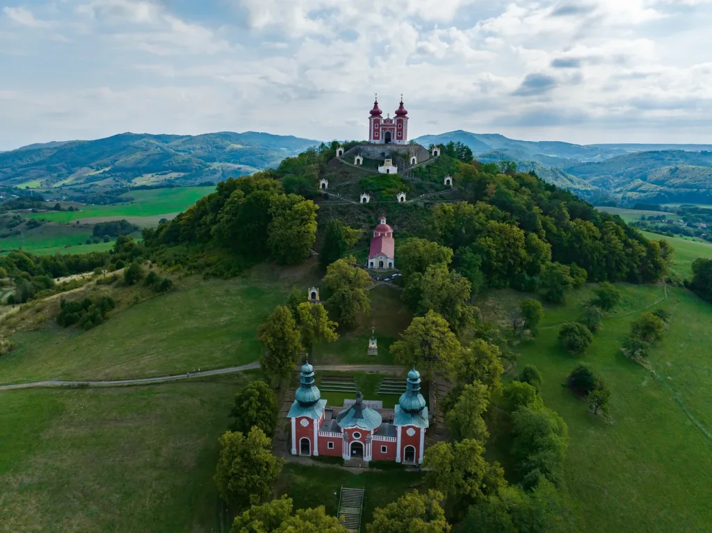 The baroque calvary at Banská Štiavnica from the air, its chapels climbing the wooded hill to the twin-towered church at the summit.
