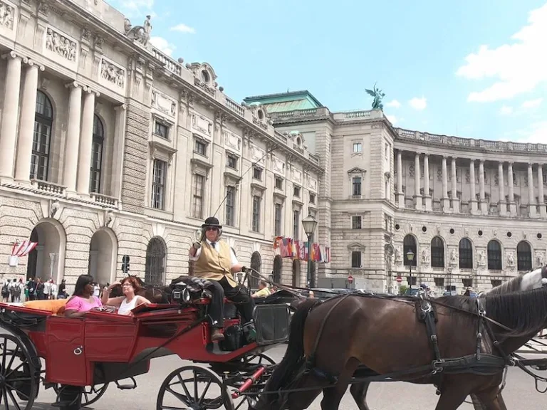 A red fiaker carriage passing the Hofburg palace in Vienna on a summer day.
