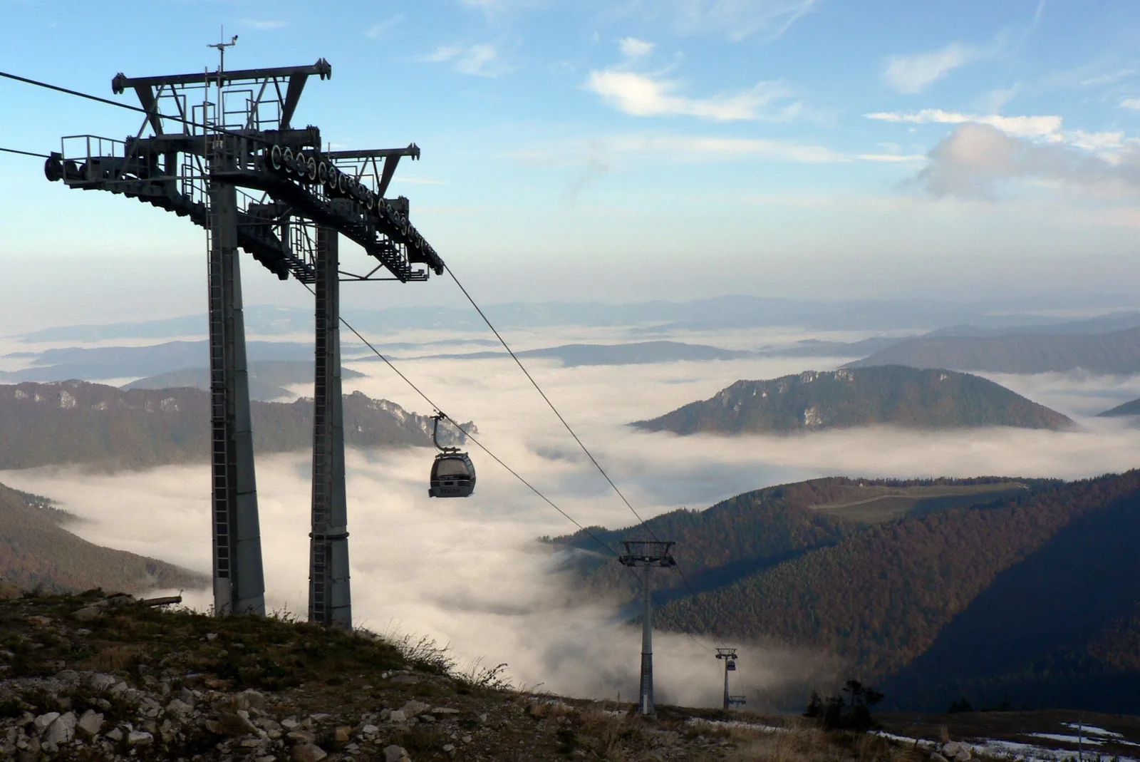 Una cabina de teleférico suspendida sobre un mar de nubes en la Malá Fatra, con las crestas del valle de Vrátna emergiendo entre la niebla.