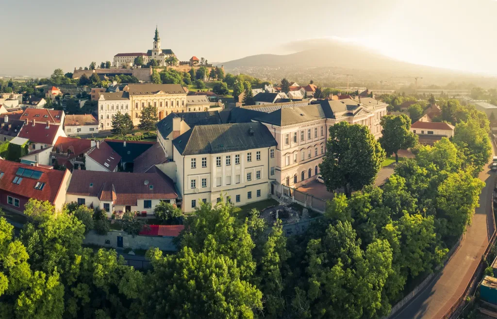 Nitra from the air at sunrise, the castle and cathedral on their hill above the old town, with Zobor Hill rising through the haze behind.