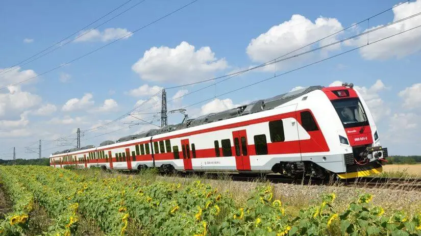 A red and white Slovak passenger train running through fields under a blue sky.