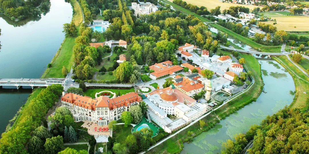 L'île thermale de Piešťany vue du ciel, avec l'hôtel Thermia Palace et le bâtiment à coupole des bains Irma dans le parc, entre le Váh et son bras secondaire.