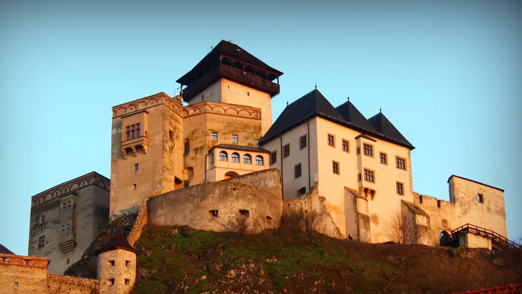 Trenčín Castle glowing in the evening sun, the Matthew Tower and the palace roofs standing above its rocky hill.