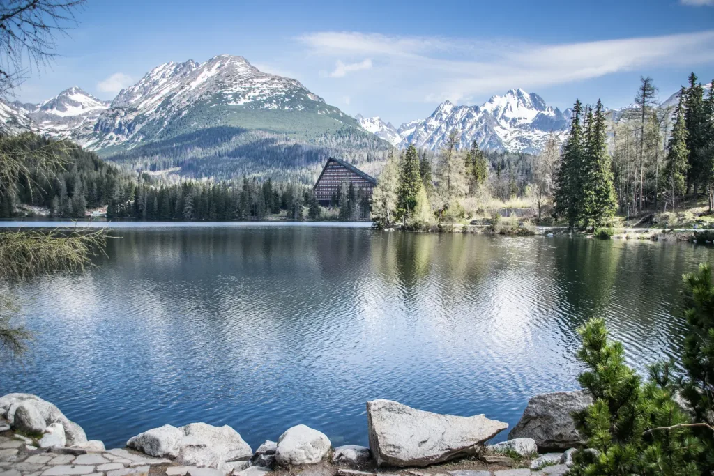 Štrbské Pleso, the glacial lake in the High Tatras, with the A-frame Hotel Patria on its shore and snow-capped peaks behind.