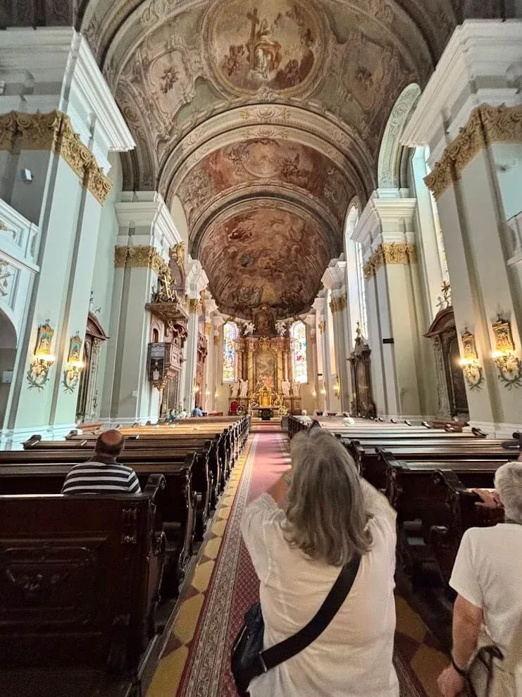 Visitors walking up the aisle of a baroque church in Banská Bystrica, its barrel vault covered in frescoes.