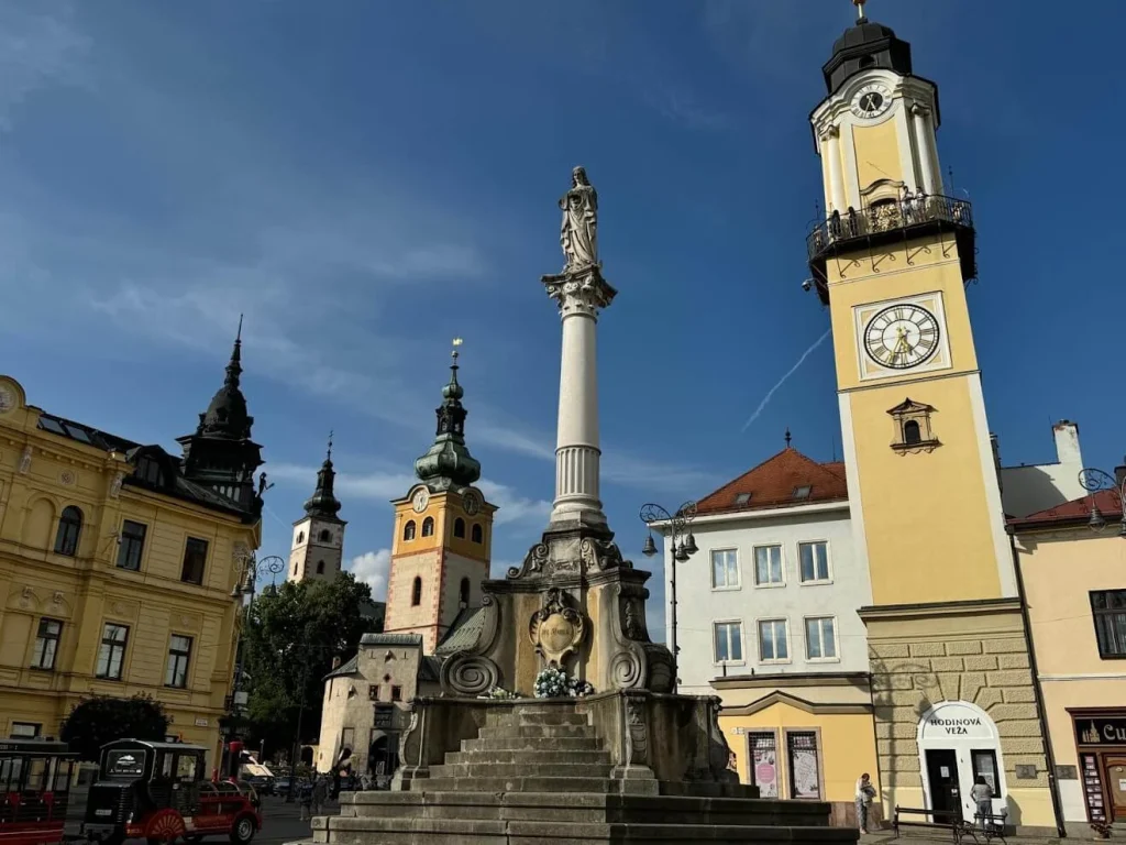 SNP Square in Banská Bystrica, with the Marian column at its centre, the yellow clock tower on the right and the castle church towers behind.
