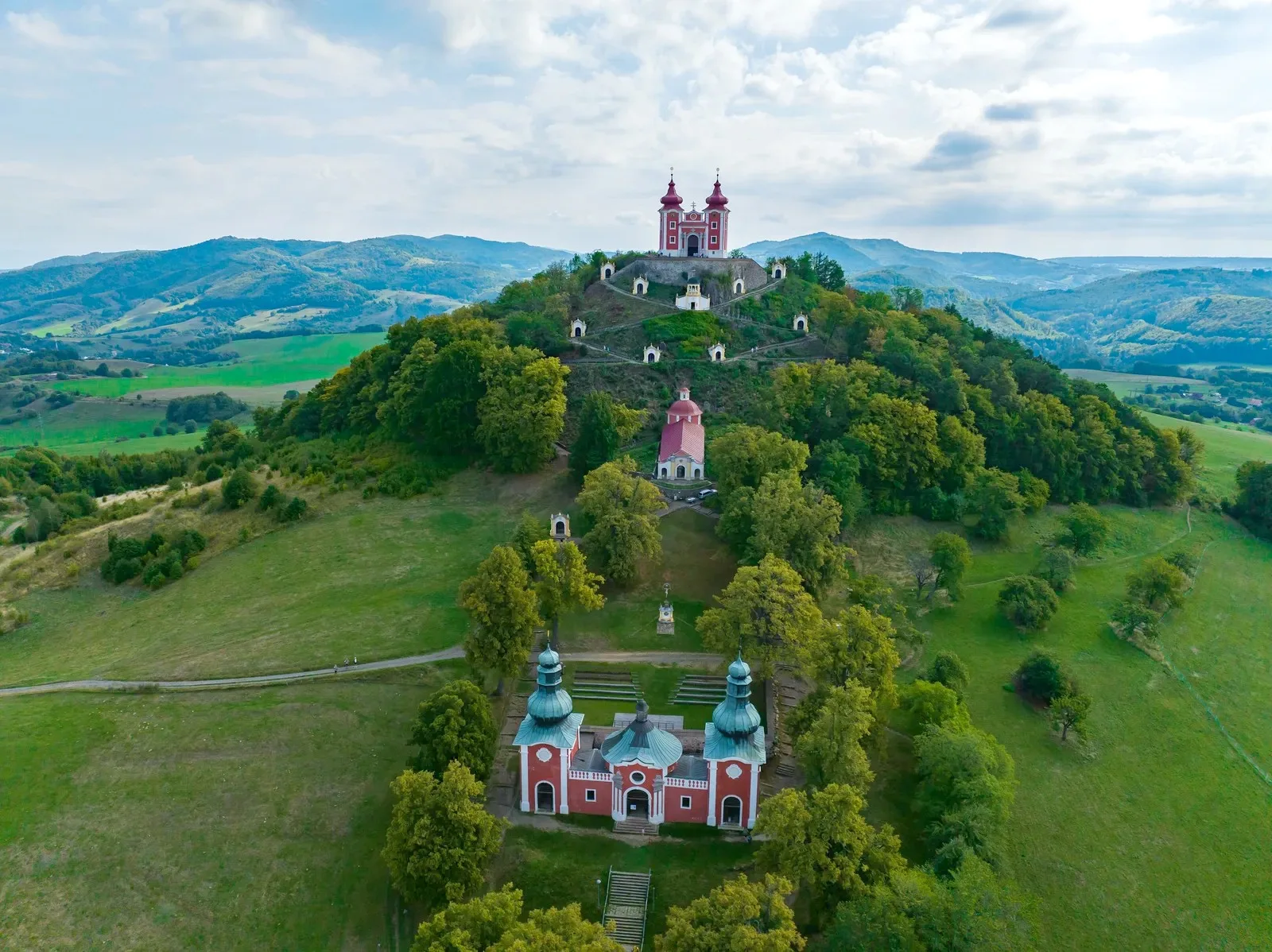Le calvaire baroque de Banská Štiavnica vu du ciel, ses chapelles blanches gravissant la colline boisée jusqu'à l'église à deux tours au sommet.