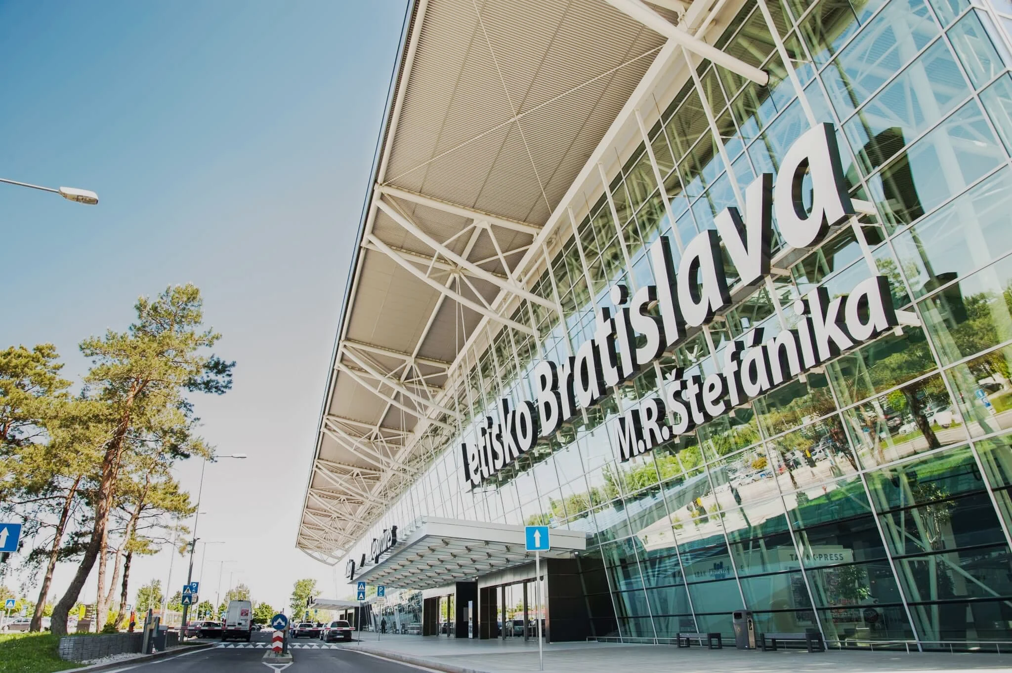 The glass front of the main terminal at M. R. Štefánik Airport in Bratislava on a clear day, carrying the sign Letisko Bratislava M. R. Štefánika above the entrance.