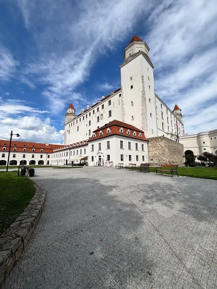 Bratislava Castle seen from its courtyard, white walls and red-roofed corner towers against a blue sky.