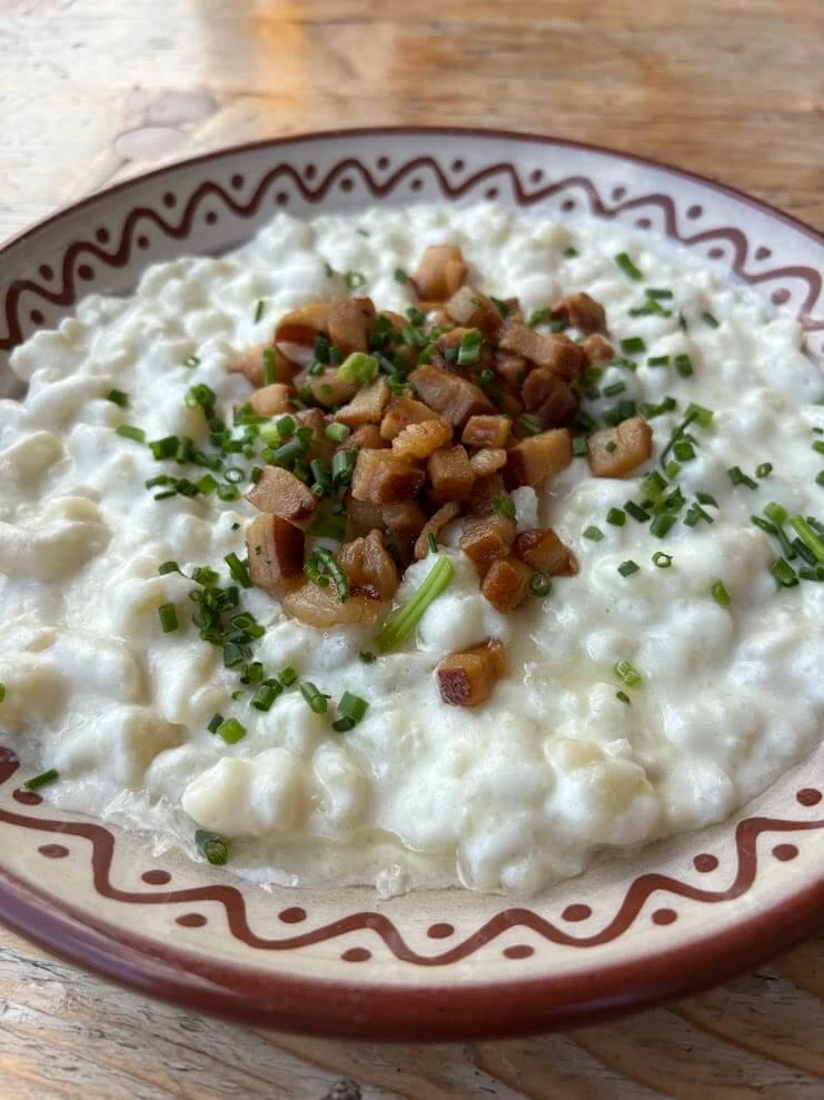 A plate of bryndzove halusky — potato dumplings with sheep cheese, bacon and chives — served on a painted folk dish.