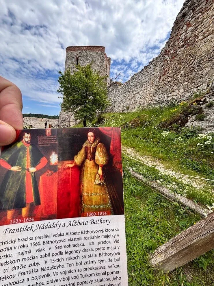 A card showing portraits of Ferenc Nádasdy and Elizabeth Báthory held up inside the walls of Čachtice Castle.