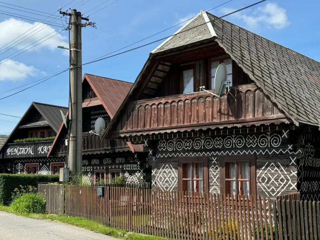 Painted log houses along a village street in Čičmany, their dark walls decorated with white folk patterns.