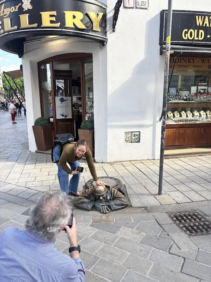 Des visiteurs photographiant la statue en bronze de Čumil qui surgit d'une bouche d'égout dans la vieille ville de Bratislava.