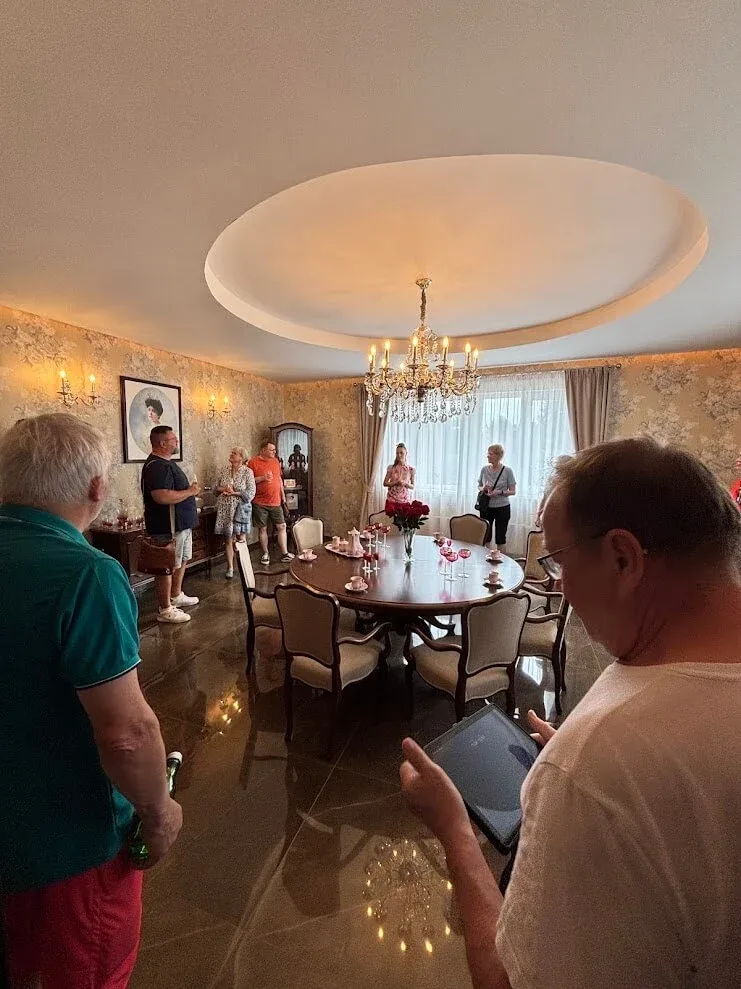 A group being shown an elegant salon with a round table, chandelier and patterned walls at the manor in Dolná Krupá.