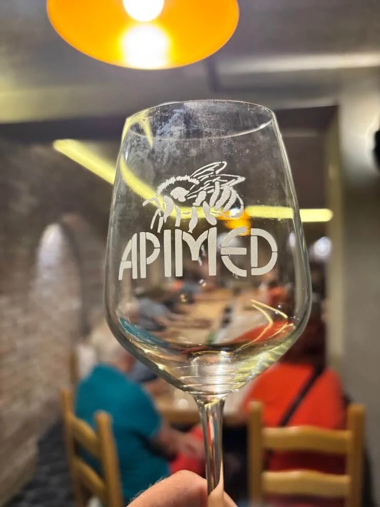 A tasting glass of mead held up in a brick-vaulted cellar at Dolná Krupá, the tasting group seated behind.