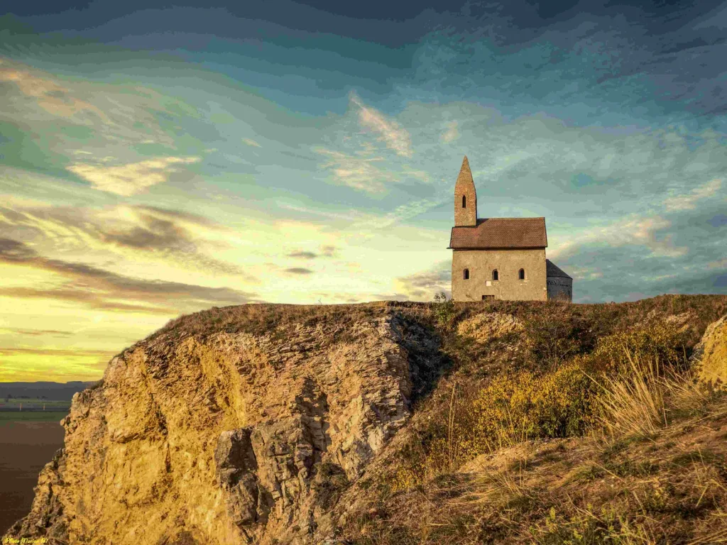 The Romanesque Church of St Michael the Archangel standing alone on its rocky hill above Dražovce at sunset.