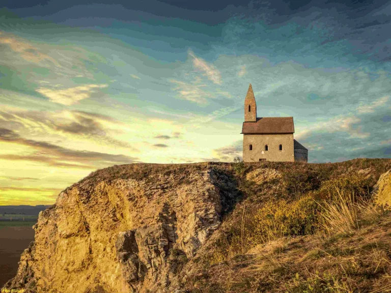 The Romanesque Church of St Michael the Archangel standing alone on its rocky hill above Dražovce at sunset.