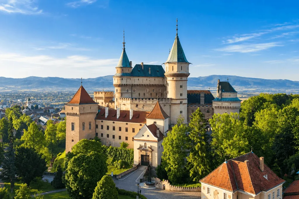 Bojnice Castle rising above the trees, with its towers and turrets and the town and hills of the Upper Nitra valley behind.