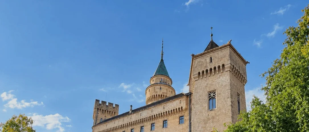 Le château de Bojnice au-dessus de son mur couvert de lierre, la tour ronde au toit vert et la tour-porte en pierre sur un ciel bleu d'automne.