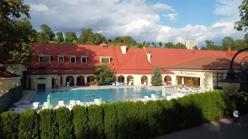 The outdoor thermal pool beside the red-roofed wellness building at the Bojnice spa, with sun loungers around the water.