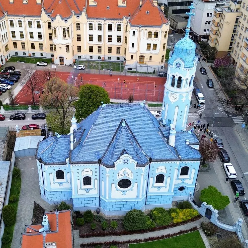 The Blue Church in Bratislava seen from the air, its blue and white tower rising above the surrounding streets.