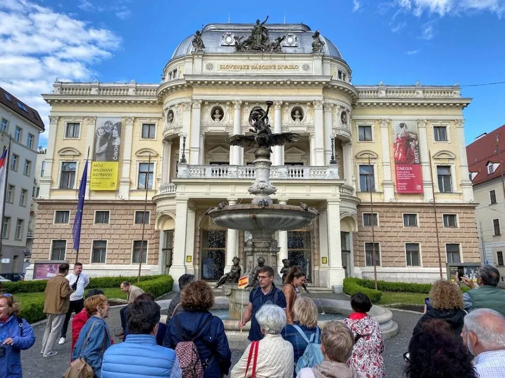 A tour group listening to their guide in front of the historic Slovak National Theatre building in Bratislava.