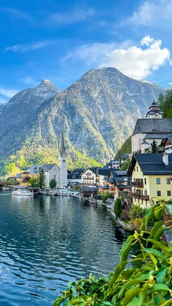 The village of Hallstatt in Austria along the shore of its lake, the church spire standing above the waterfront houses with steep Alpine slopes rising behind.
