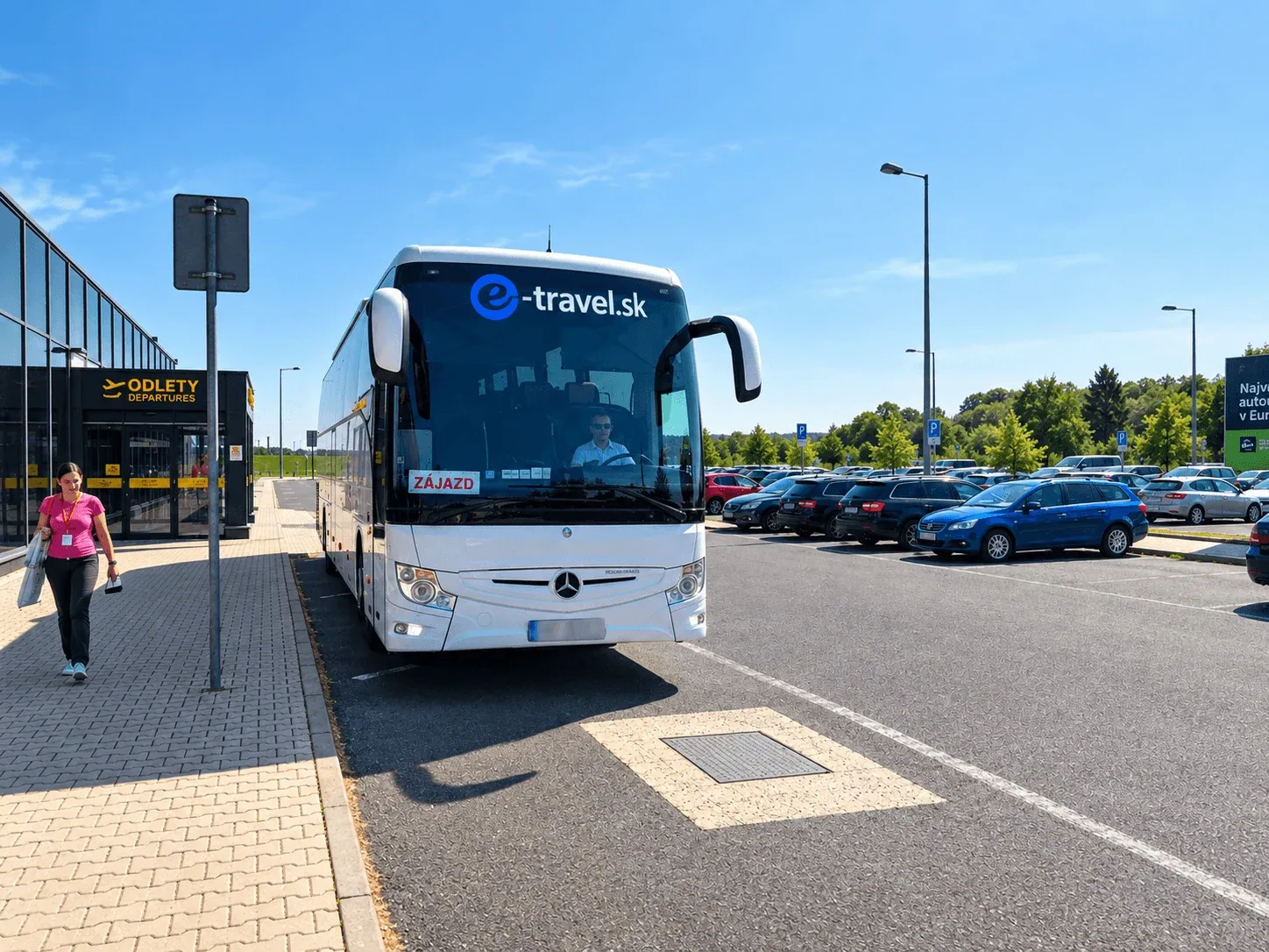 Ein Reisebus von e-travel.sk wartet an einem klaren Sommertag am Abflugeingang des Flughafens Poprad-Tatry, mit dem Flughafenparkplatz dahinter.