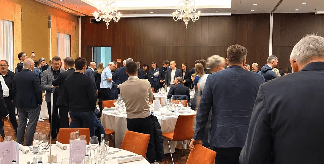 Des invités circulant entre les tables d'un dîner de gala d'entreprise dans une salle de bal d'hôtel éclairée par des lustres.