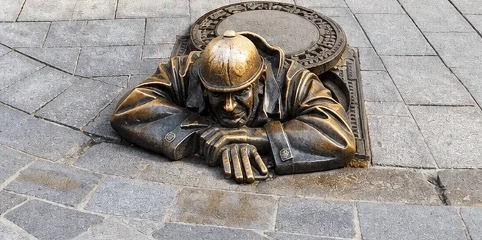Čumil, the bronze Man at Work statue, leaning out of a manhole in the cobbled street of Bratislava Old Town.