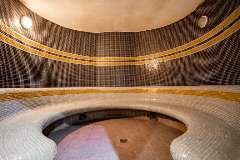 A guest in the indoor thermal pool at the spa in Dudince, with autumn trees outside the tall windows.