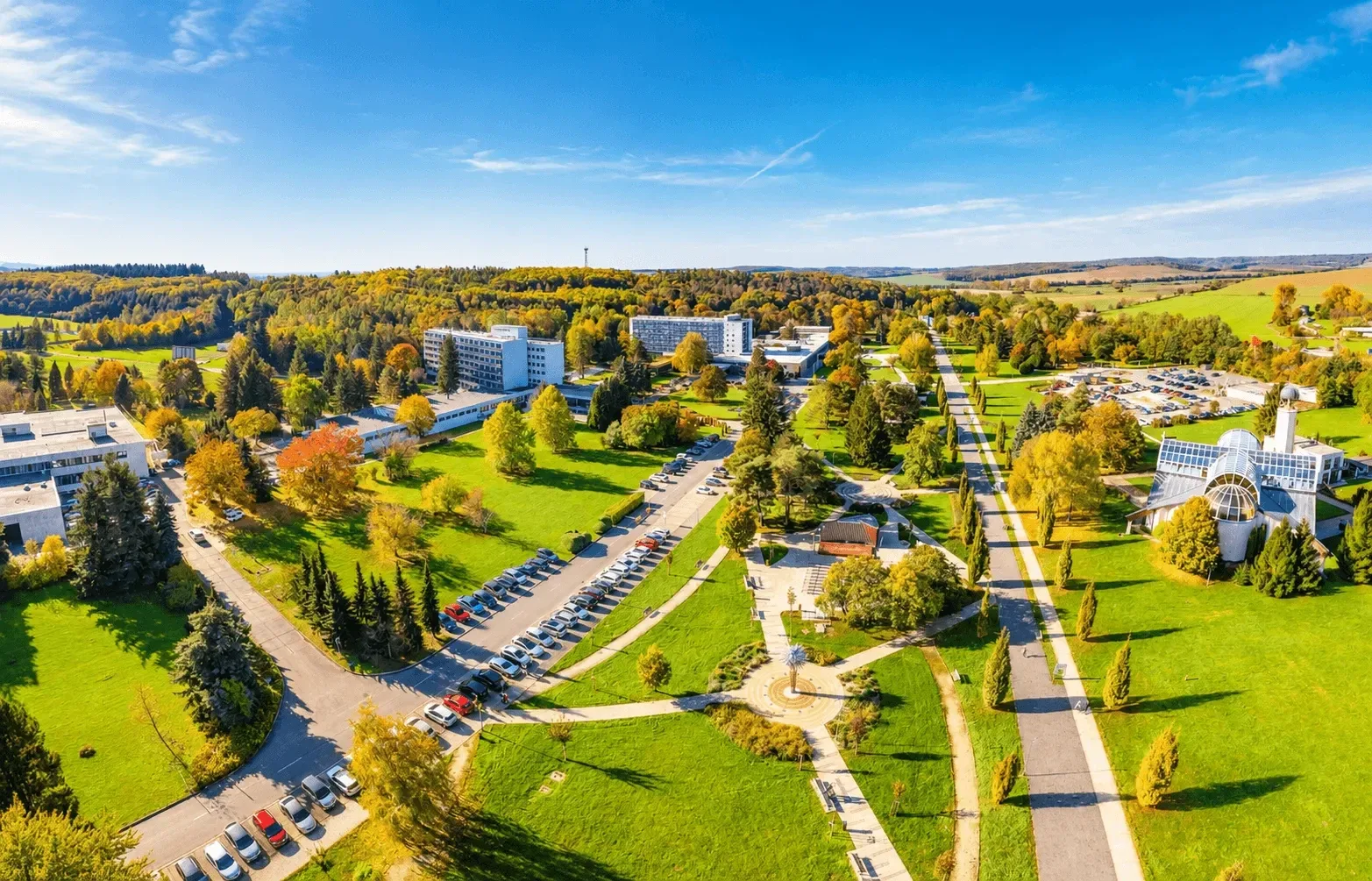 An aerial view of the spa quarter in Dudince in autumn, with spa hotels, lawns and tree-lined paths surrounded by woods and fields.