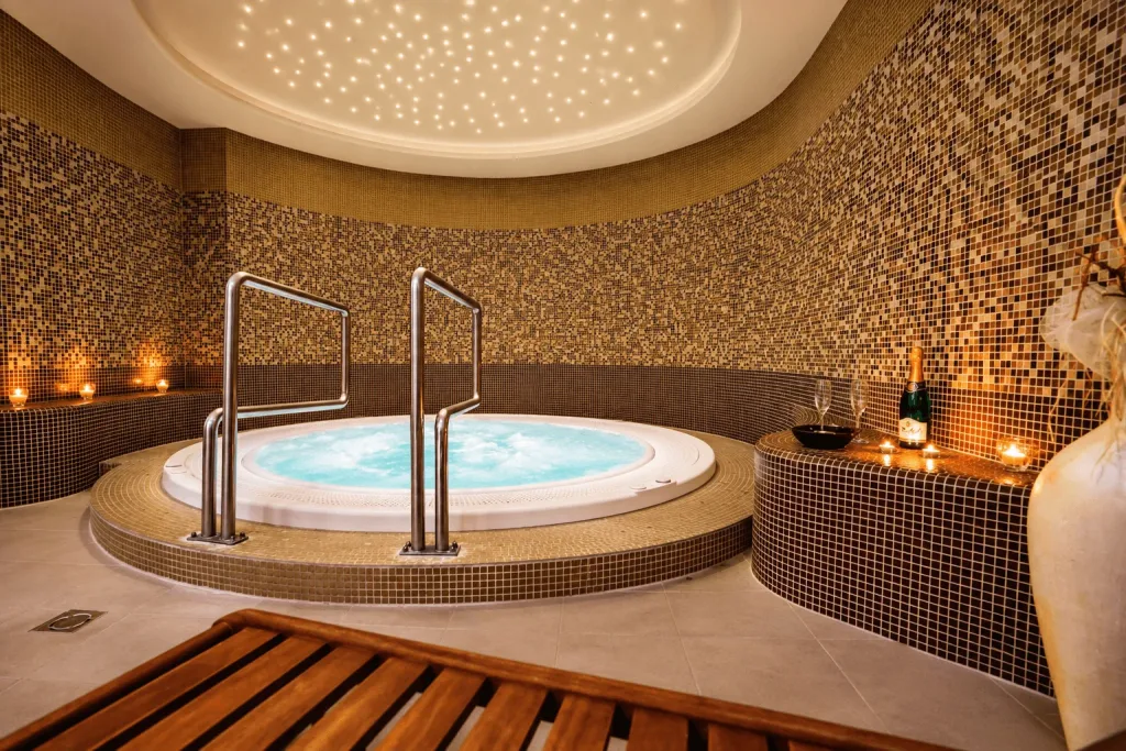 A whirlpool in a mosaic-tiled spa room in Dudince, lit by candles under a starlit ceiling.