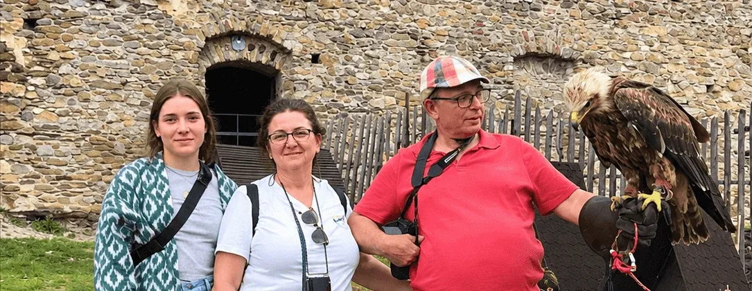 Tre visitatori accanto a un falconiere che tiene un’aquila sul guanto, davanti alle mura di pietra di un castello in Slovacchia.