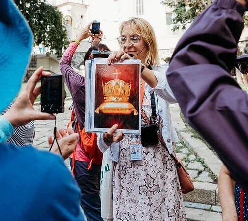 Una guida che mostra a un gruppo un’immagine della Sacra Corona d’Ungheria durante un tour a piedi nella Città Vecchia di Bratislava, accanto a una chiesa gotica.
