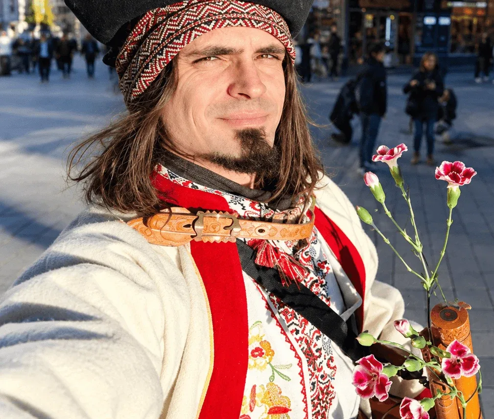 Un guía vestido con traje tradicional de pastor eslovaco, con camisa bordada, un instrumento de madera tallado y claveles, para una visita temática por la ciudad.