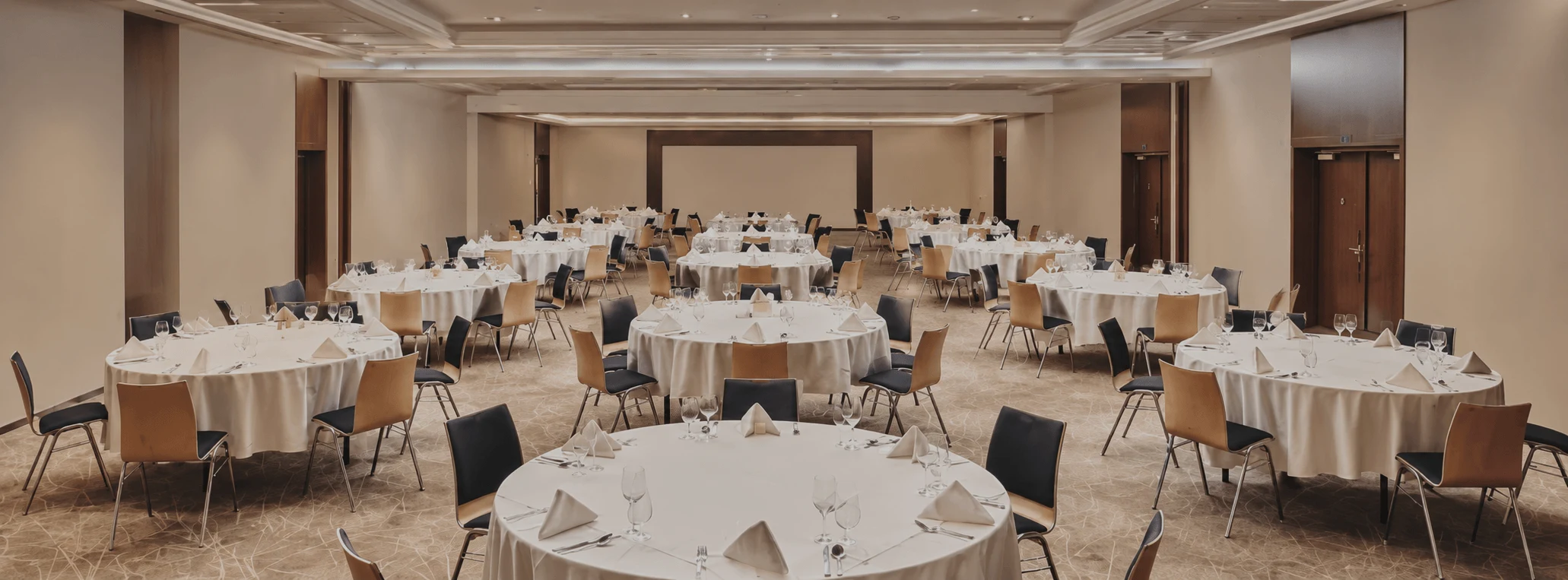 Une salle de bal d'hôtel aménagée pour un dîner de gala, avec des tables rondes dressées de nappes en lin blanc et de verrerie.