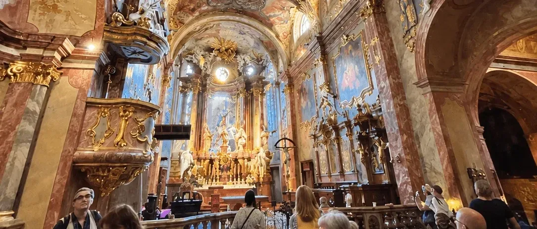Visitors inside a baroque church in Nitra, with the gilded high altar, carved pulpit and frescoed vaults.
