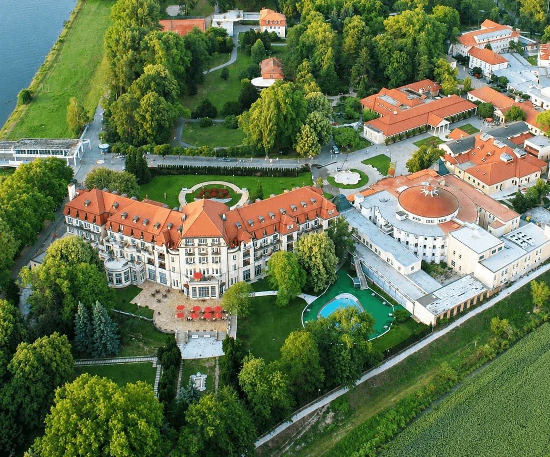 Вид с воздуха на Курортный остров в Пьештянах рядом с рекой Ваг: отель Thermia Palace и курортное здание Irma с куполом среди деревьев парка.