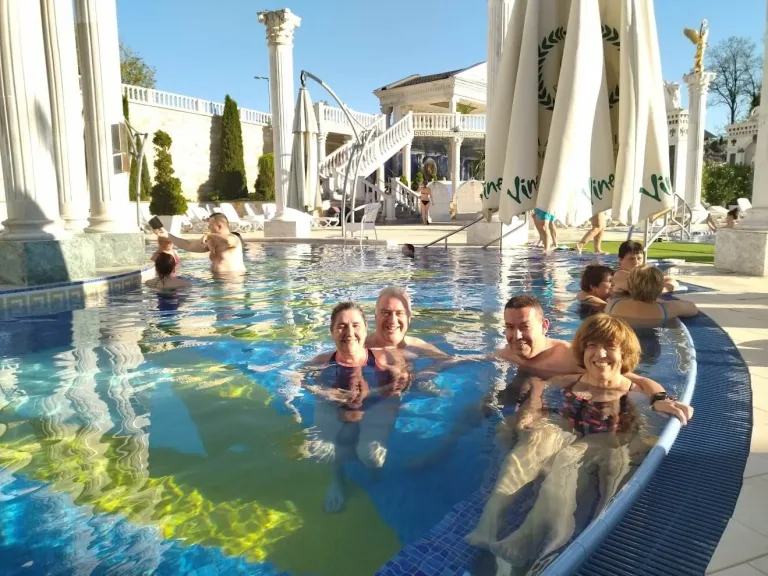 Guests relaxing in the outdoor thermal pool at the Aphrodite spa in Rajecké Teplice, among white columns and balustrades.