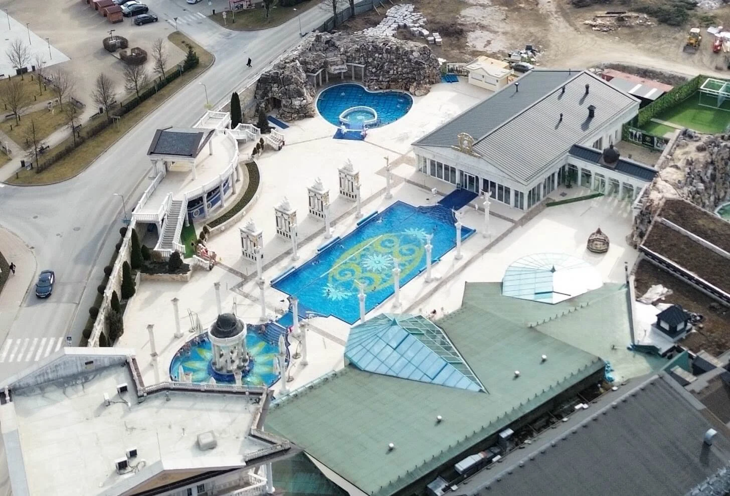 An aerial view of the outdoor thermal pools at the Aphrodite spa in Rajecké Teplice, lined with white columns and classical pavilions.