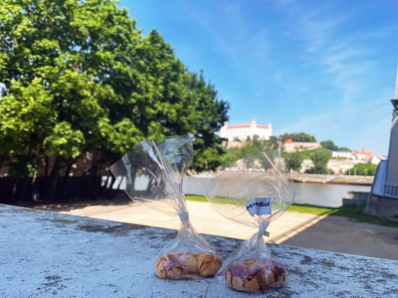 Deux pâtisseries emballées posées sur un muret au bord du Danube, avec le château de Bratislava sur sa colline de l'autre côté du fleuve.