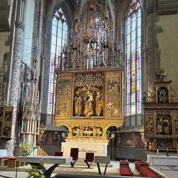 A tall carved gothic altar under the vaulted ceiling of a church, lit by stained-glass windows.