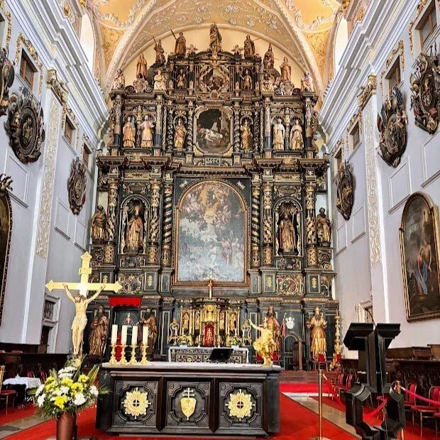 The towering carved and gilded baroque high altar of the Cathedral of St John the Baptist in Trnava, with a crucifix and flowers at the altar table below it.